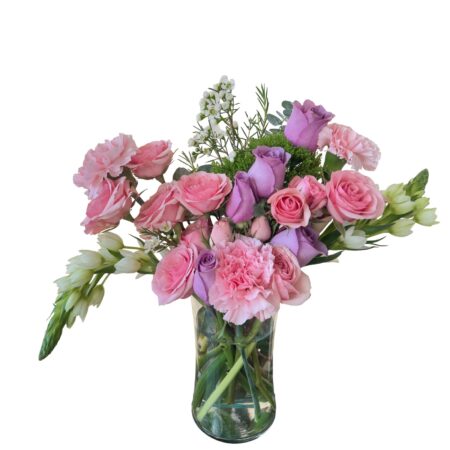 This floral arrangement from L’amour Floral Designs is a cheerful mix of soft pink and lavender roses, light pink carnations, delicate white blooms, and lush greenery displayed in a clear glass vase. The colors are balanced beautifully, evoking a romantic and uplifting tone perfect for springtime occasions or heartfelt sentiments. The arrangement is fresh, airy, and feminine, ideal for expressing love, appreciation, or warm wishes.