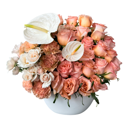 A modern and elegant floral arrangement presented in a white ceramic bowl, featuring a lush blend of peach roses, apricot spray roses, beige carnations, creamy white lisianthus, and two white anthuriums as sculptural accents. This warm-toned bouquet offers a refined, designer look—ideal for stylish gifting, upscale décor, or meaningful celebrations.
