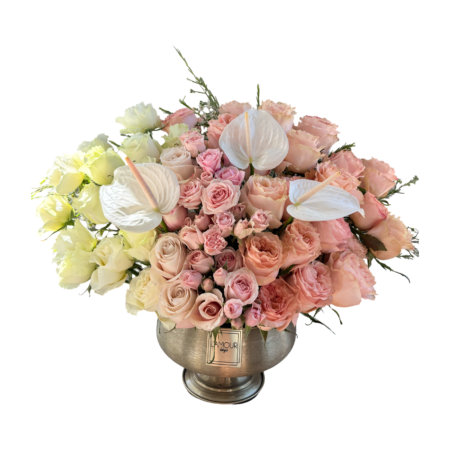 A sophisticated floral arrangement in a silver pedestal vase from L’amour Designs, featuring a soft palette of blush pink, ivory, and white. The bouquet includes blush roses, pink spray roses, white roses, and sculptural white anthurium flowers. This polished and refined design radiates luxury and serenity, perfect for upscale gifting and romantic gestures.