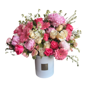 A generous, pastel-toned floral arrangement in a white cylindrical L’amour Floral Designs hatbox, overflowing with soft pink and ivory blooms. The bouquet features pink peonies, ivory and blush roses, coral spray roses, pink gerbera daisies, white stock, and assorted seasonal greenery. This elegant and dreamy arrangement is ideal for romantic celebrations, heartfelt milestones, and feminine gifting occasions.