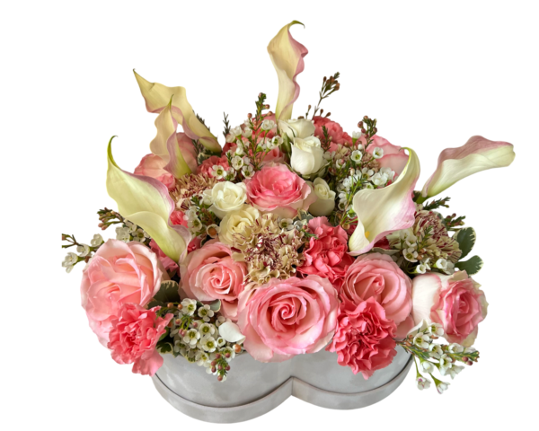 A delicate floral arrangement presented in a white heart-shaped hatbox, featuring elegant ivory calla lilies, blush and coral roses, light pink carnations, cream spray roses, and white waxflowers. With its soft curves and gentle pastel palette, this design radiates love, tenderness, and timeless beauty—ideal for romantic gestures, anniversaries, and thoughtful gifts.