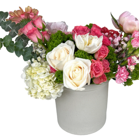 A charming pastel floral arrangement presented in a matte off-white ceramic vase, featuring ivory roses, white tulips, pale green hydrangeas, blush peonies, pink gerbera daisies, pink carnations, spray roses, baby’s breath, and pops of green moss filler and eucalyptus. This design blends elegance and freshness—perfect for romantic gestures, spring celebrations, or heartfelt messages of love and support.