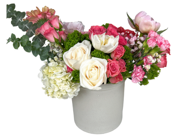 A charming pastel floral arrangement presented in a matte off-white ceramic vase, featuring ivory roses, white tulips, pale green hydrangeas, blush peonies, pink gerbera daisies, pink carnations, spray roses, baby’s breath, and pops of green moss filler and eucalyptus. This design blends elegance and freshness—perfect for romantic gestures, spring celebrations, or heartfelt messages of love and support.